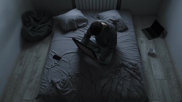 Sadness and pain after breakup. Young man sitting on bed holding photo of ex girlfriend, hugging it tightly, feeling deep pain and loneliness.