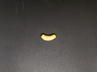 A single piece of uncooked elbow macaroni on a textured black surface