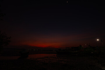 A captivating scene of a wrecked ship lying aground on a muddy shore under a bright sunset sky. The...