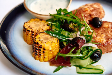 A Vibrant Culinary Presentation featuring Grilled Corn, Fresh Greens, and Savory Protein Served with a Creamy Dip on an Elegant Plate