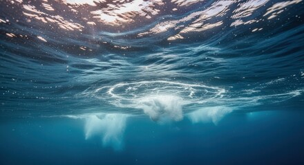 Underwater view of a breaking wave. Sunlight illuminates a swirling, frothy impact below the surface of deep blue water