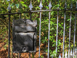 Old classical style black metal letter box hanging on a wrought iron fence on the exterior of a residential property