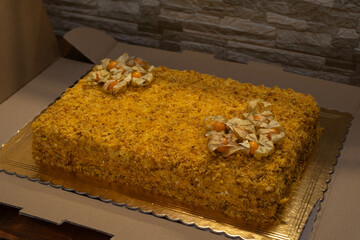 Homemade Napoleon cake decorated with physalis berries, placed on a golden tray in cardboard packaging. Perfect image for bakery, dessert, celebration, or catering service-themed stock collections.