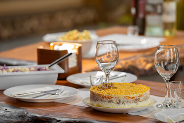 Festive table setting with a traditional Russian layered salad Mimosa made with fish, eggs, and vegetables. Holiday meals, Slavic cuisine, celebratory dining concept.