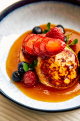 A Delightful Plated Dessert Featuring Fluffy Pancakes Topped with Fresh Strawberries, Raspberries,...