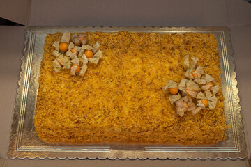 Homemade Napoleon cake decorated with physalis berries, placed on a golden tray in cardboard packaging. Perfect image for bakery, dessert, celebration, or catering service-themed stock collections.