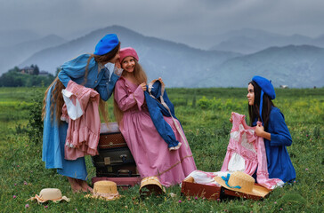 Dreamy vintage girl in blue dress reading a book on stacked suitcases in countryside field under cloudy sky