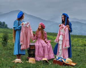 Dreamy vintage girl in blue dress reading a book on stacked suitcases in countryside field under cloudy sky
