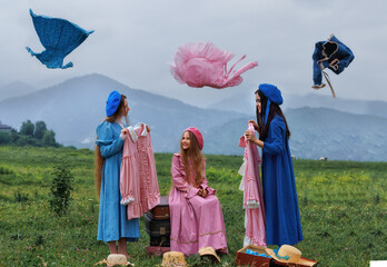 Dreamy vintage girl in blue dress reading a book on stacked suitcases in countryside field under cloudy sky