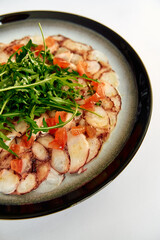 A beautifully arranged plate featuring thinly sliced octopus with fresh tomatoes and arugula, highlighting vibrant colors and exquisite culinary presentation.
