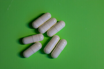 White capsules are scattered on a bright green background, creating a simple yet appealing...