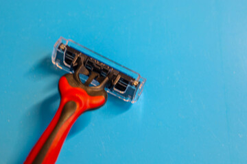 A razor with a red and black handle and a transparent protective cover on the blade is positioned on a blue background.