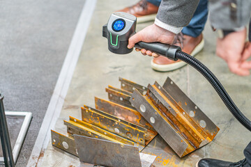 A candid image showing a person using a laser anti-corrosion tool on rusty metal pieces on a...