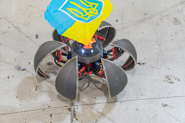 Indoor scene of a fallen drone with flag, debris scattered around Blue and yellow flag text unclear...