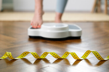 Young woman weighing on scale with a measuring tape in foreground