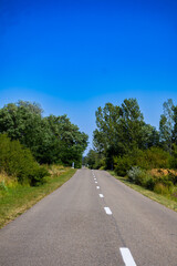 A rural road stretches ahead, its white dashed line leading into a tranquil vanishing point. Green...