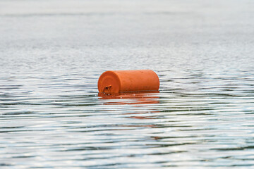 A red life preserver floats on calm waters, possibly near the shore. The setting is overcast with...