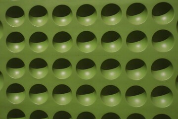 Close-up of a green plastic surface with circular cut-out pattern, creating a repetitive grid...