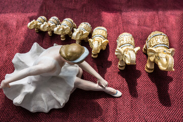 Porcelain figurine of a ballerina in a white tutu and seven bone Indian elephants lined up on red cloth. Vintage still life of retro items of our grandmothers - nostalgic background, top view.