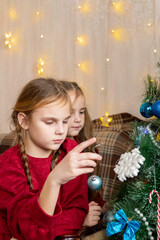 Little sisters, beautiful child girls in red dresses are decorating a Christmas tree in living room. winter New Year's concept.