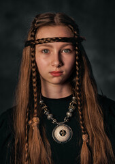 Mystical portrait of young girl with tribal braids and ethnic jewelry in dark background