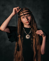 Mystical portrait of young girl with tribal braids and ethnic jewelry in dark background