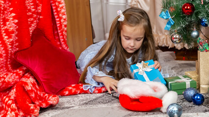 Little children enjoying Christmas, sisters lying on the floor and looking at boxes. Happy...