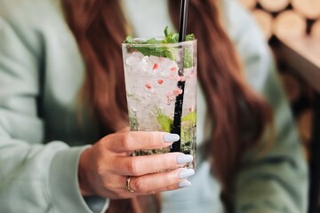 Unrecognizable Woman holding refreshing drink with mint and ice in cozy outdoor sitting.