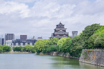 広島城とそのお堀を、曇り空と新緑とともに収めた風景。広島市の街並み