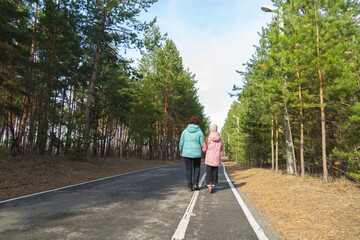 Little girl riding scooter while walking with her grandmother in the forest on a sunny day