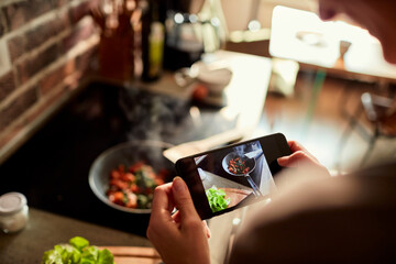 Young woman using a smart phone to take a photo of a meal she is cooking and preparing in the kitchen