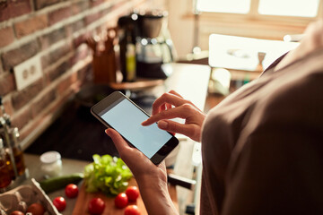 Young woman using a smart phone while cooking and preparing a healthy meal