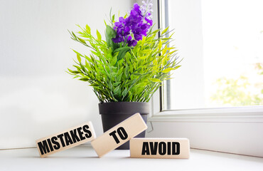 A message to avoid is written on wooden blocks in a composition with a plant on the windowsill.