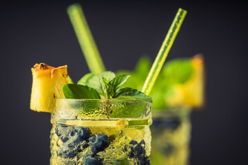 Refreshing mojito cocktail with pineapples and blueberry on the rustic background. Selective focus.