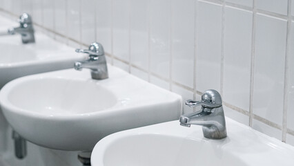 Public bathroom with white ceramic sinks and chrome faucets on clean wall