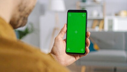 Over the shoulder close up of a man holding a smartphone with a blank chroma key green screen, a perfect mock up for mobile apps or websites.