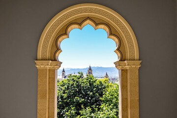 Fototapeta premium Ornate arched window frames a scenic cityscape and distant mountains.