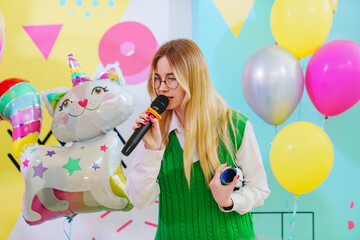 A funny young woman with a microphone is leading a children's party.