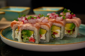 Artfully arranged sushi roll featuring salmon, avocado, cream cheese, and garnished with onion bits on a stylish plate, ideal for discerning culinary enthusiasts.