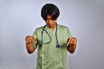 Young Male Healthcare Professional Wearing Green Scrubs and Stethoscope Pointing Downward in...
