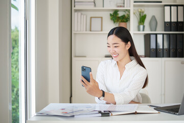 Smiling businesswoman using smartphone while working at a modern office desk