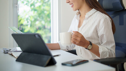 Smiling businesswoman holding a cup of coffee reading financial documents at her desk.