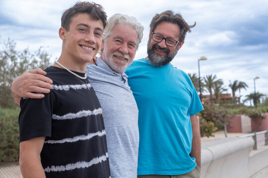 Portrait of a carefree family group of three multigenerational people, father, son and nephew smiling together outdoors by the seaside feeling joy, freedom and vacation - Powered by Adobe