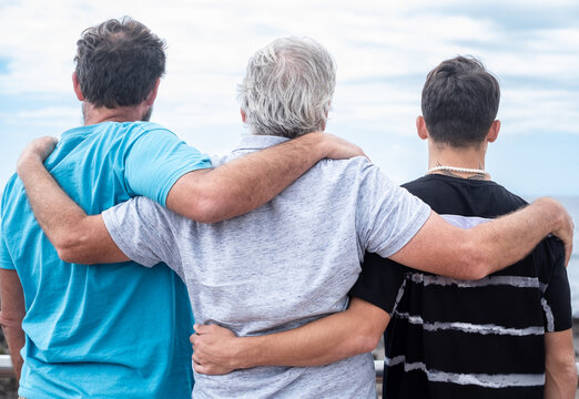 Rear view of a family group of three multigenerational people, father, son and nephew together outdoors by the seaside feeling affection, care, freedom and vacation