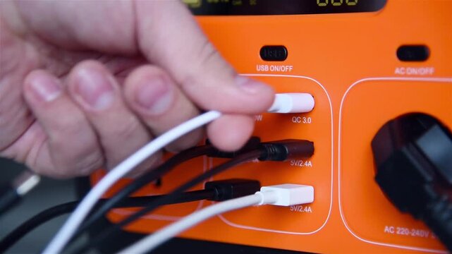 The hand turns off the portable charging station and pulls out all the wires. Technology and backup energy concept.