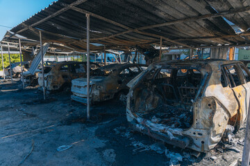 Burnt carcasses covered in ash and mud show twisted metal and melted structures. Destroyed car...