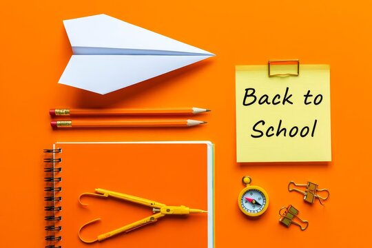 Paper airplane, sticky note with text BACK TO SCHOOL and different stationery on orange background. - Powered by Adobe