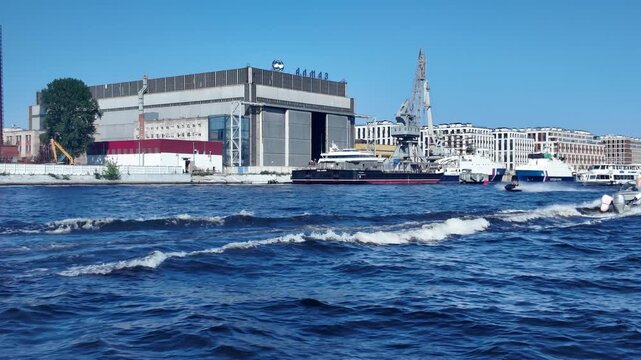 A boat speeds along the Neva River past the Almaz shipyard on a clear sunny day - St. Petersburg, Russia, July 16, 2025