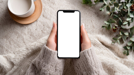 Woman holding blank smartphone screen mockup in cozy sweater lifestyle setting
