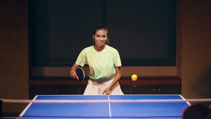 Indian young adult gen z athlete woman lady hold racket play table tennis game with man enjoy indoor dark room happy female girl learn ping pong male guy teach passing ball have fun joy spend time - Powered by Adobe